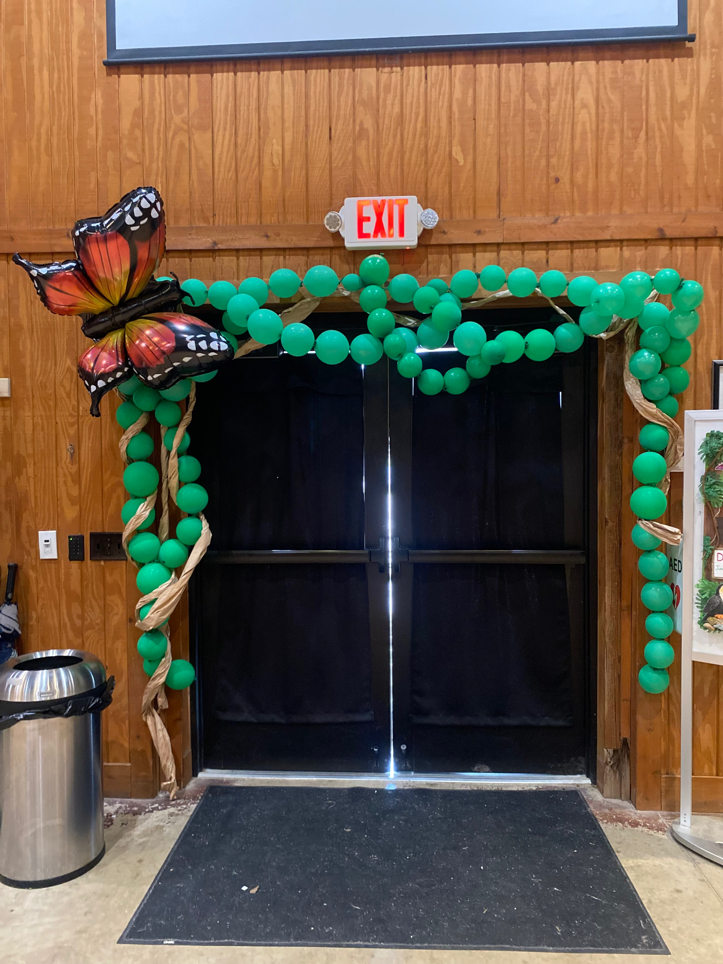 Green balloon arch with monarch butterfly foil framing a doorway for a jungle-themed corporate event