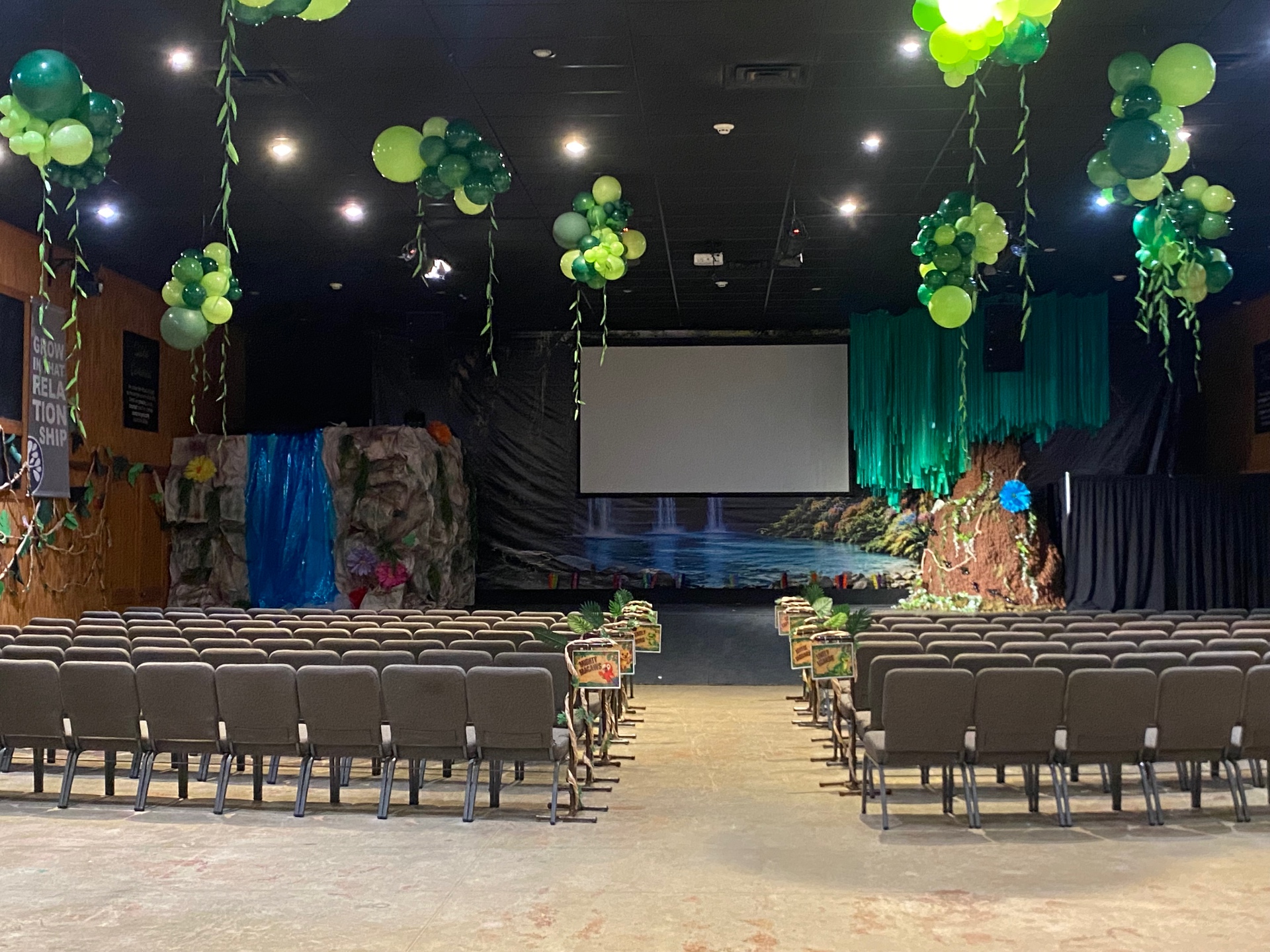 Corporate venue transformed with hanging green balloon vines and jungle stage décor