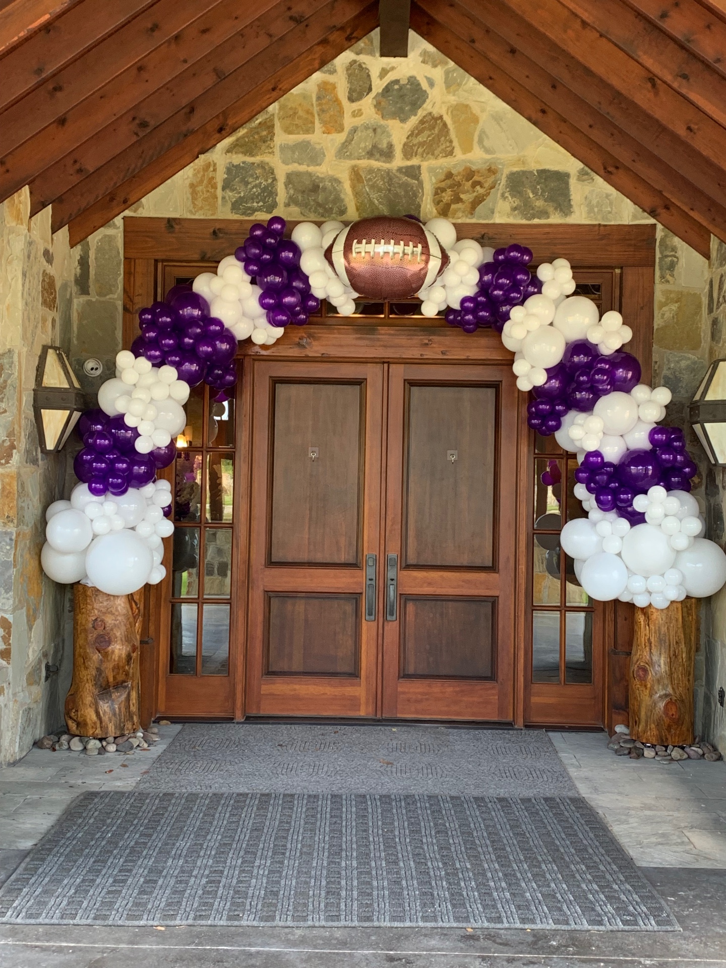 Purple and white organic balloon garland with football foil accent framing wooden double doors for the Anna Quarterback Club Dinner