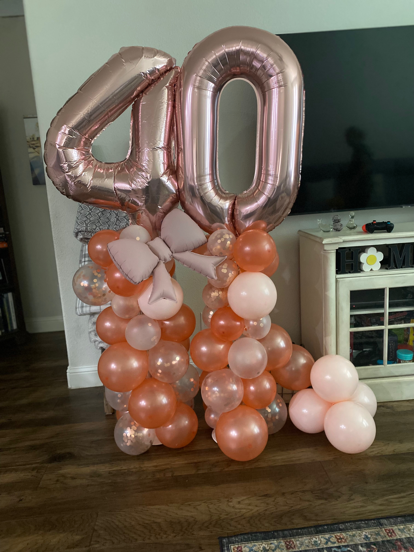 Rose gold 40th birthday balloon column with bow and peach confetti accents
