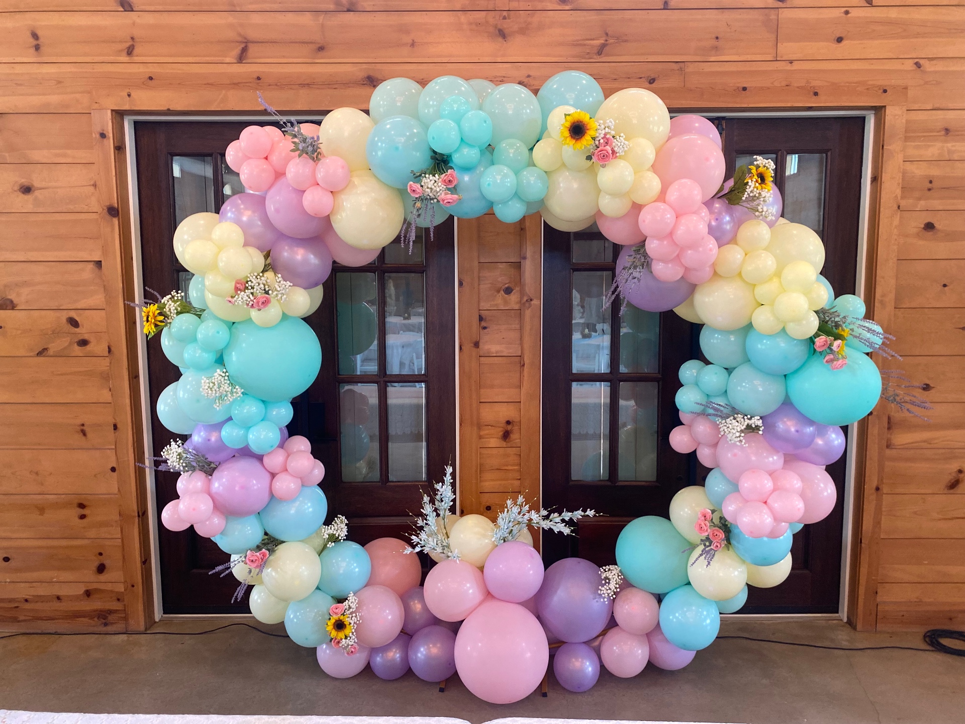 Pastel rainbow organic circle balloon arch with florals in front of wooden doors