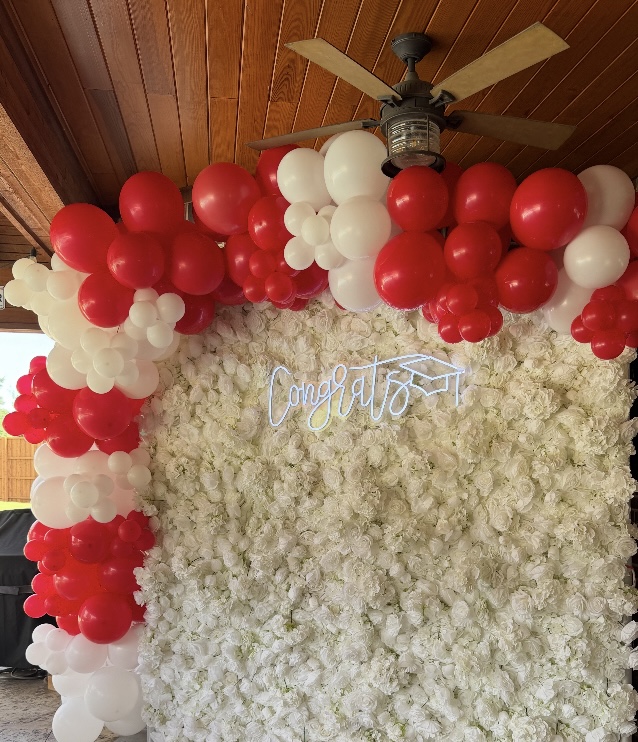 Red and white balloon garland over floral wall for graduation