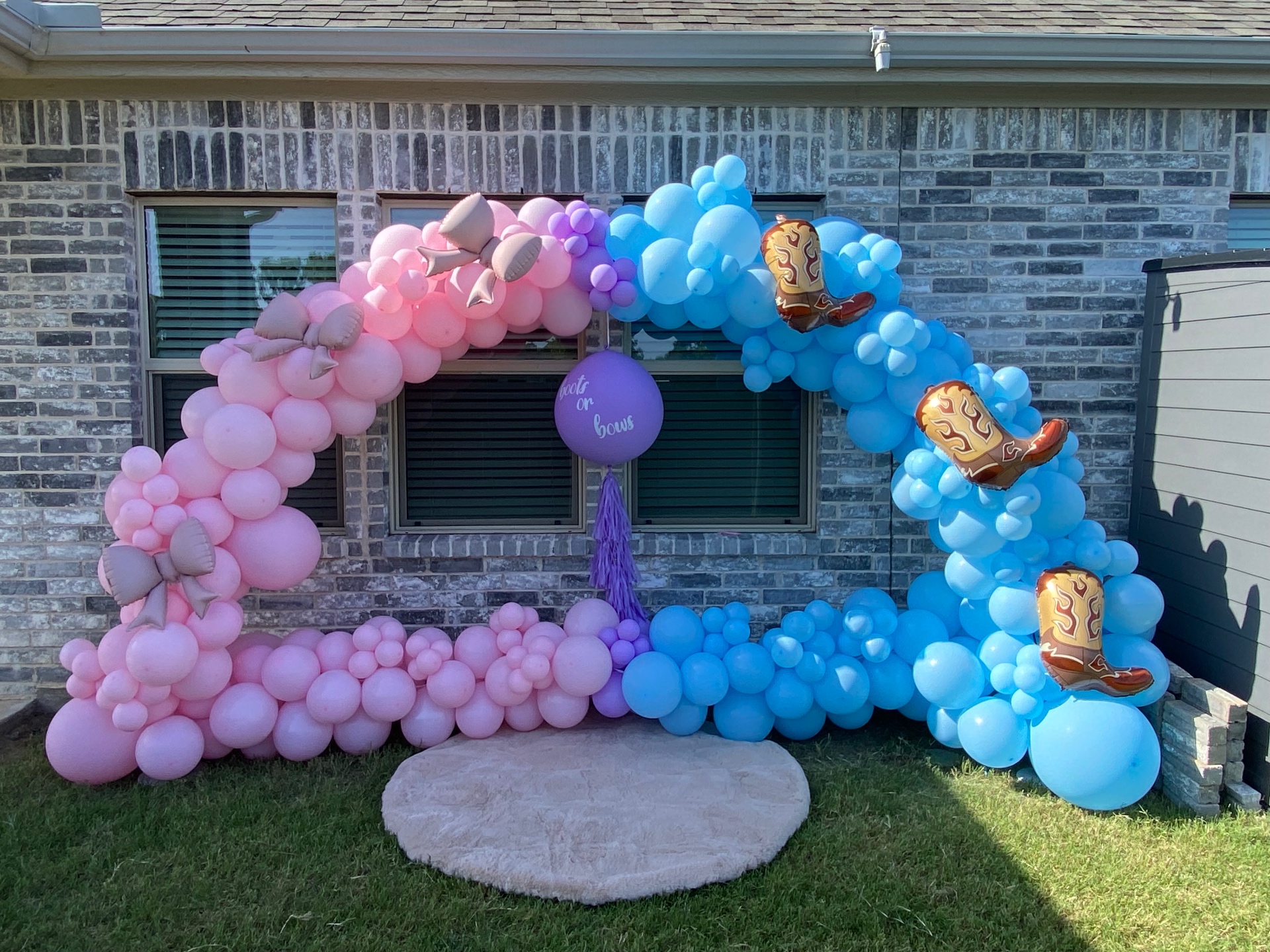 Pink and blue organic balloon arch with cowboy boots for a boots or bows gender reveal